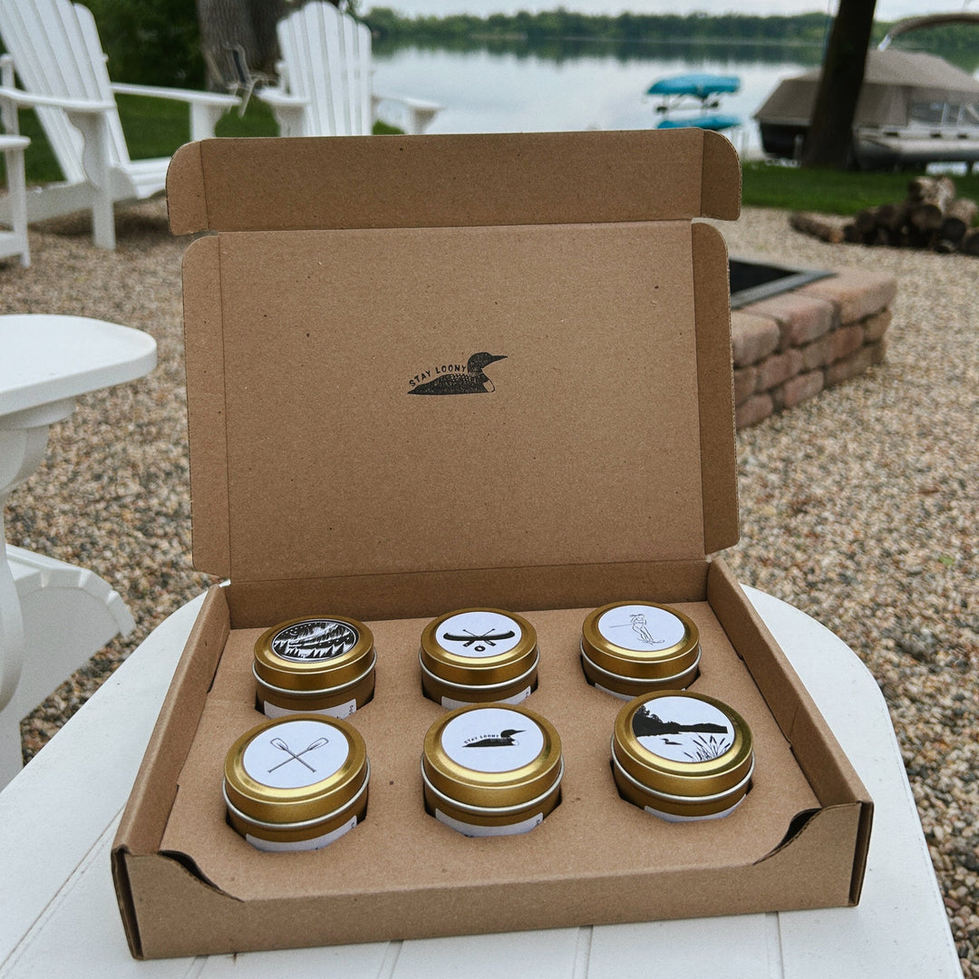 six pack of lake life candle tins on table by fire pit